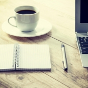 Notebook, coffee, and laptop on table.