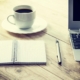 Notebook, coffee, and laptop on table.